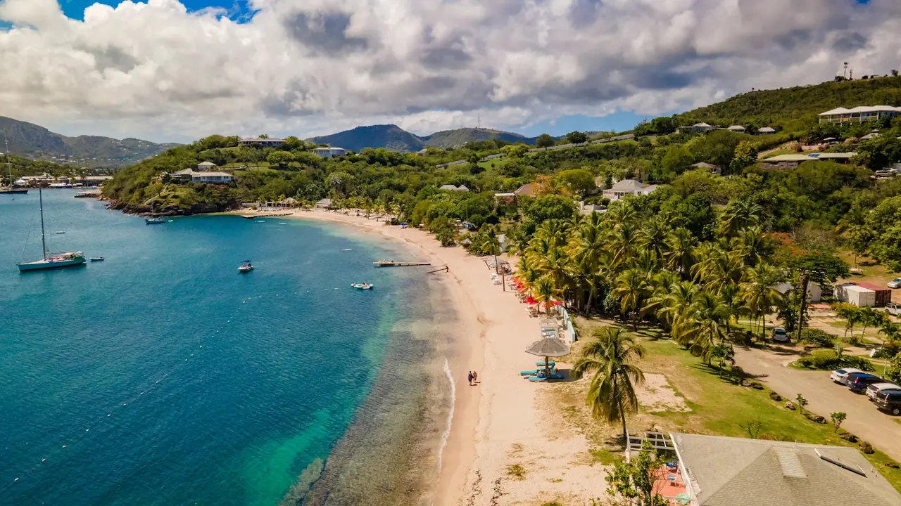 A curved sandy bay in Antigua with anchored sailboats and green hills behind