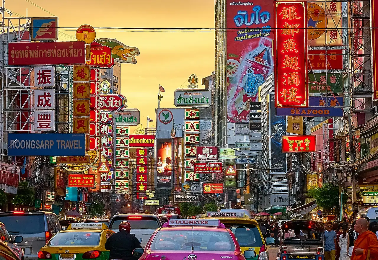 Yaowarat Road in Bangkok's Chinatown at dusk, stacked with illuminated signs above the traffic