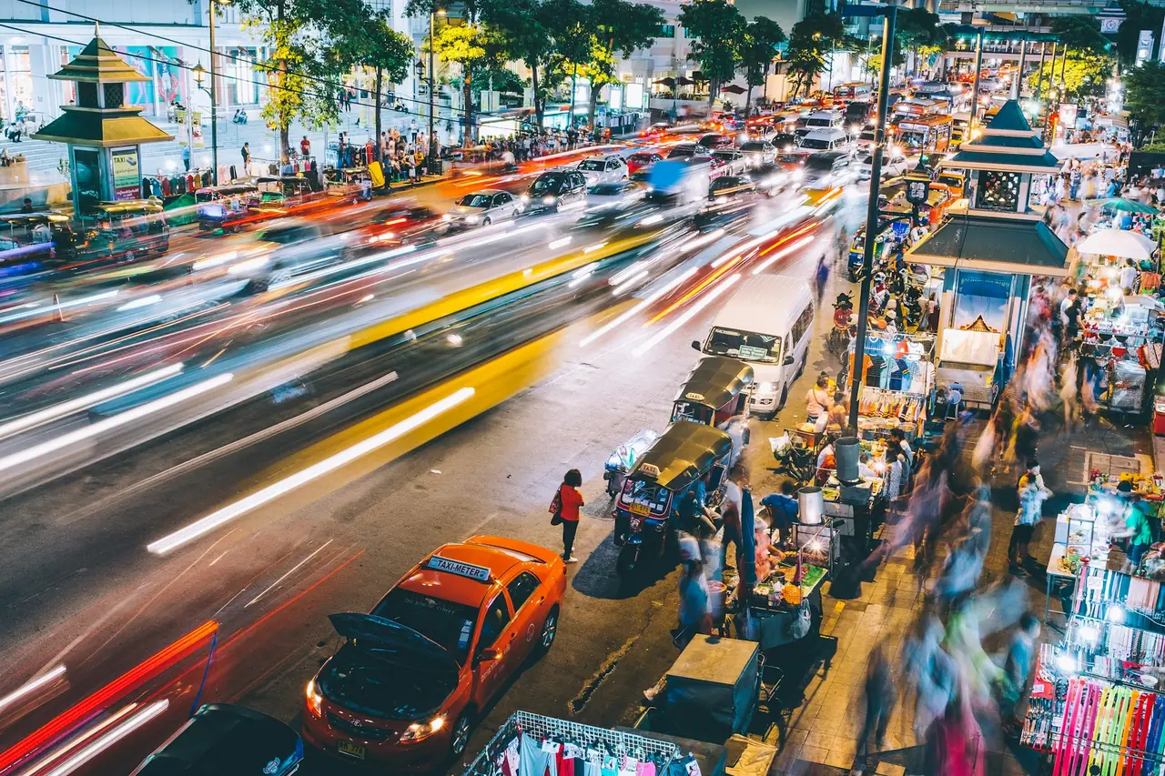 Bangkok market stalls from above at night, traffic streaking past in a long exposure