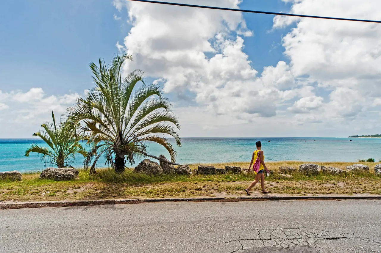 A person walking alone along a Barbados coast road beside the sea