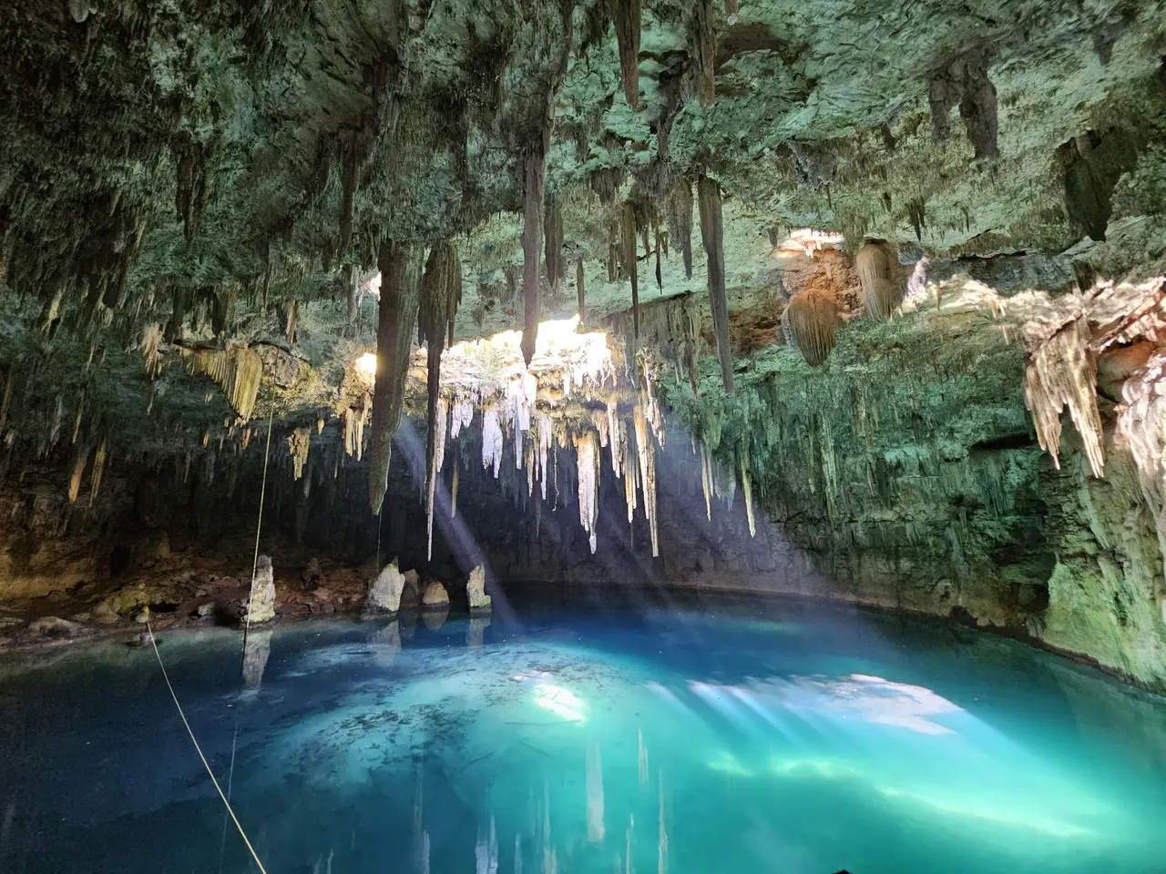 A cenote near Cancún, its pool lit blue beneath a limestone cavern hung with stalactites