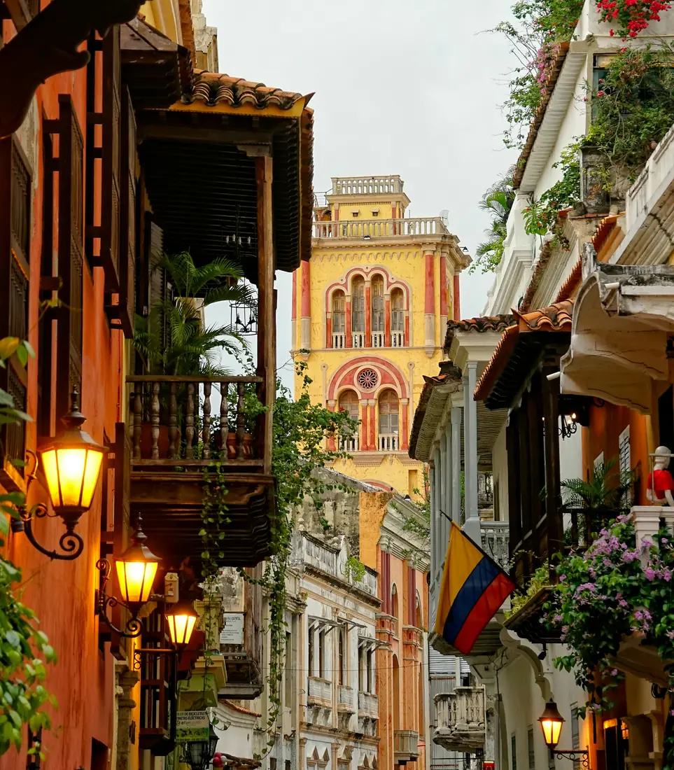 A balcony draped in flowers on a colourful street in Cartagena's walled city at dusk