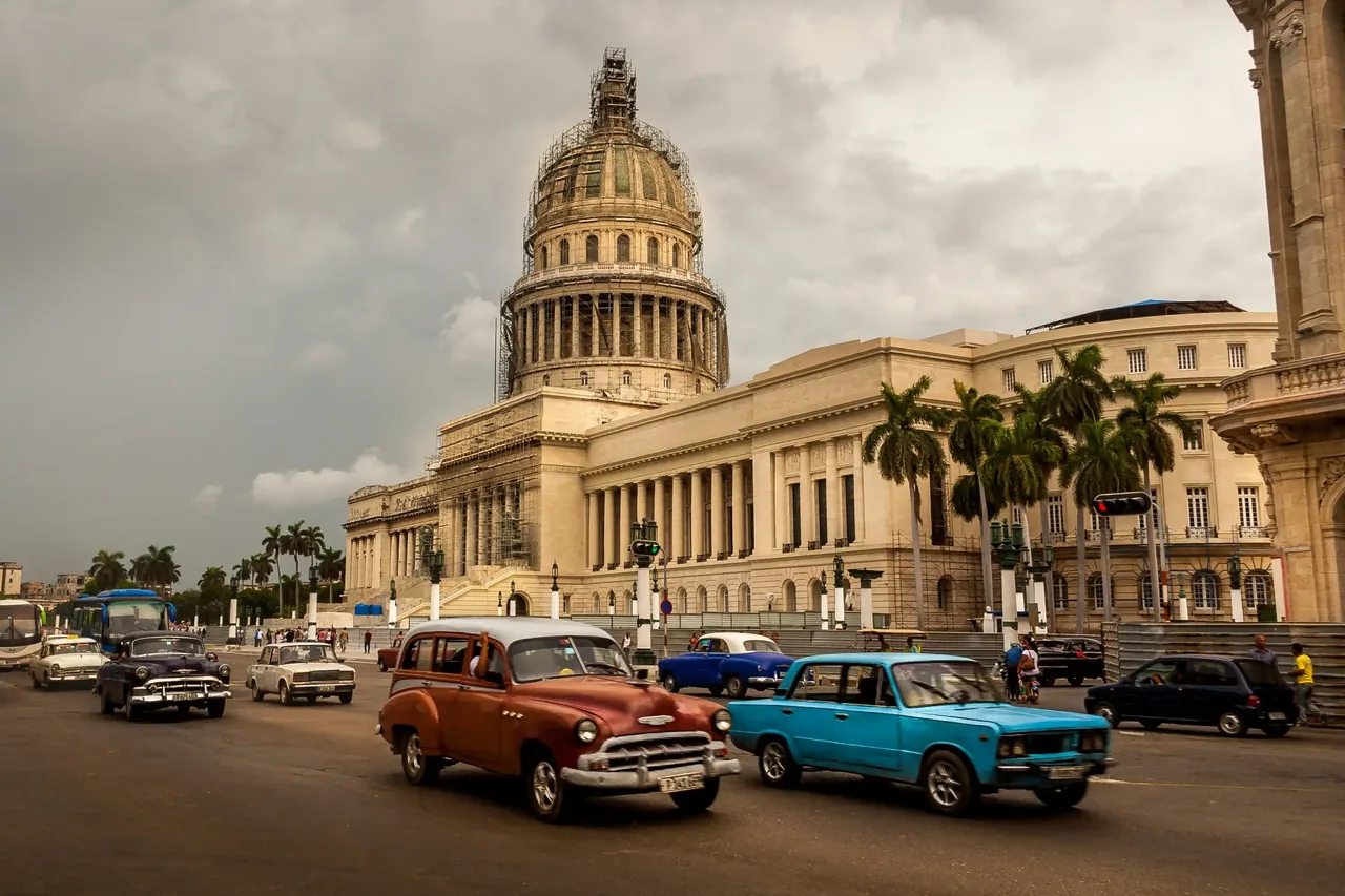 Vintage American cars parked and driving past the domed Capitolio building in Havana