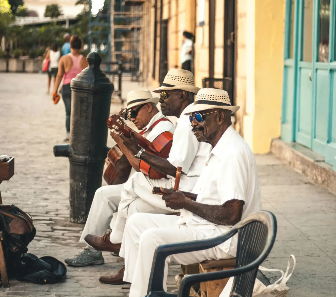 Three musicians in white shirts and straw hats playing guitar on a Havana street corner