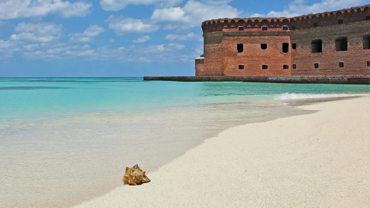 The brick walls of Fort Jefferson rising behind an empty beach and clear shallows, Dry Tortugas