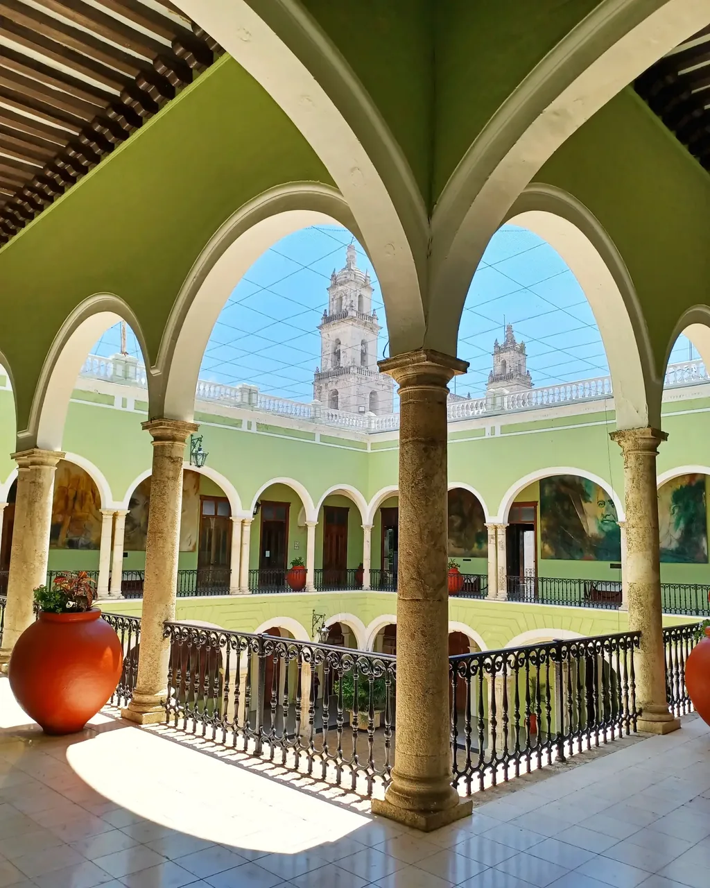 Arched colonnades around a courtyard in central Mérida, with the cathedral towers beyond