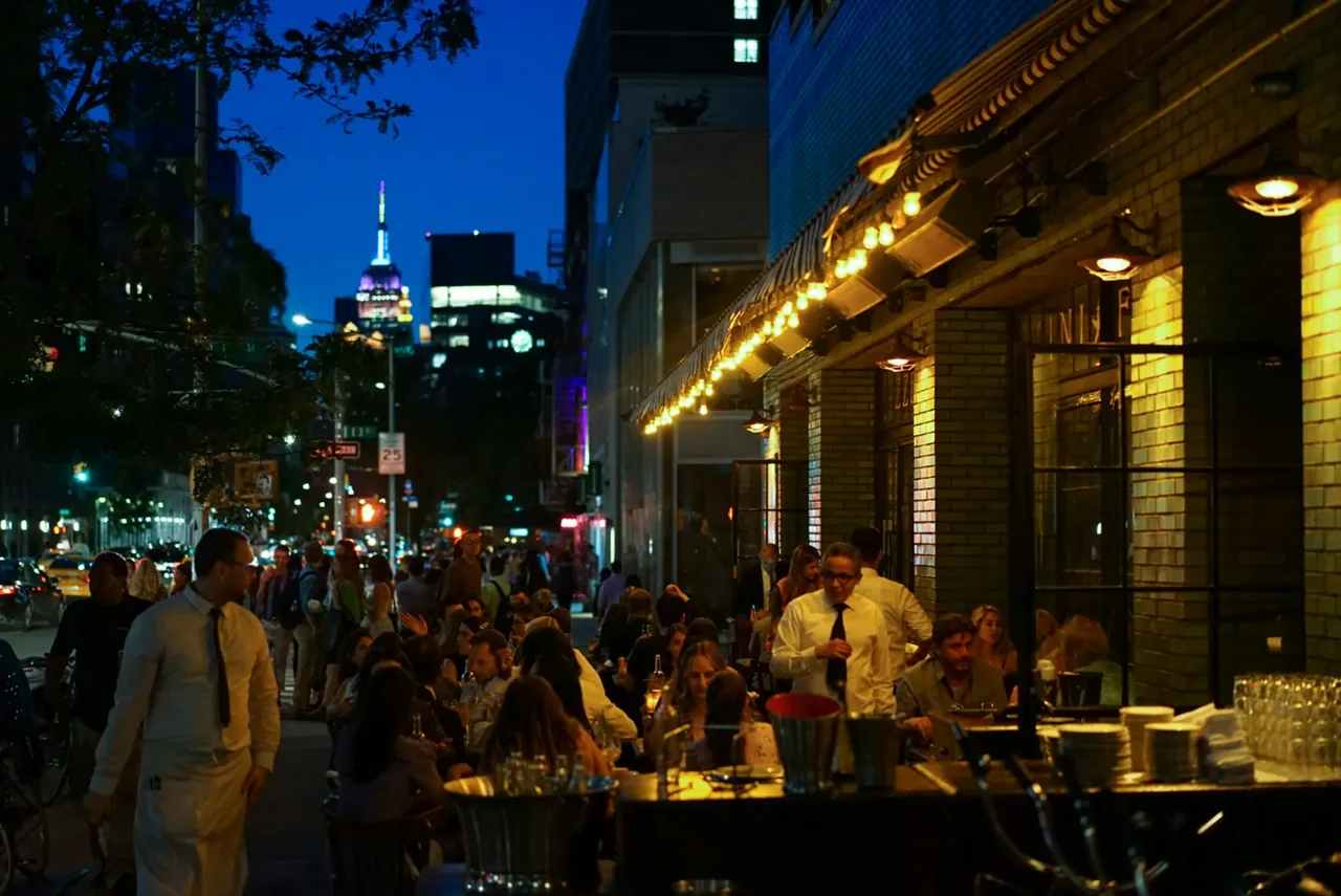 Crowded outdoor restaurant tables under warm lights on a New York street at blue hour