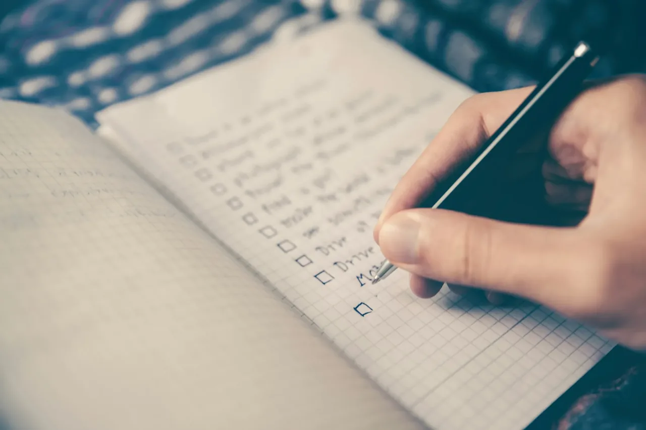 A hand writing a list in pencil in a lined notebook
