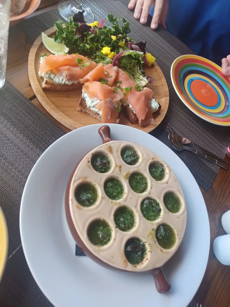 A plate of escargots and a plate of smoked salmon on a restaurant table, seen from above