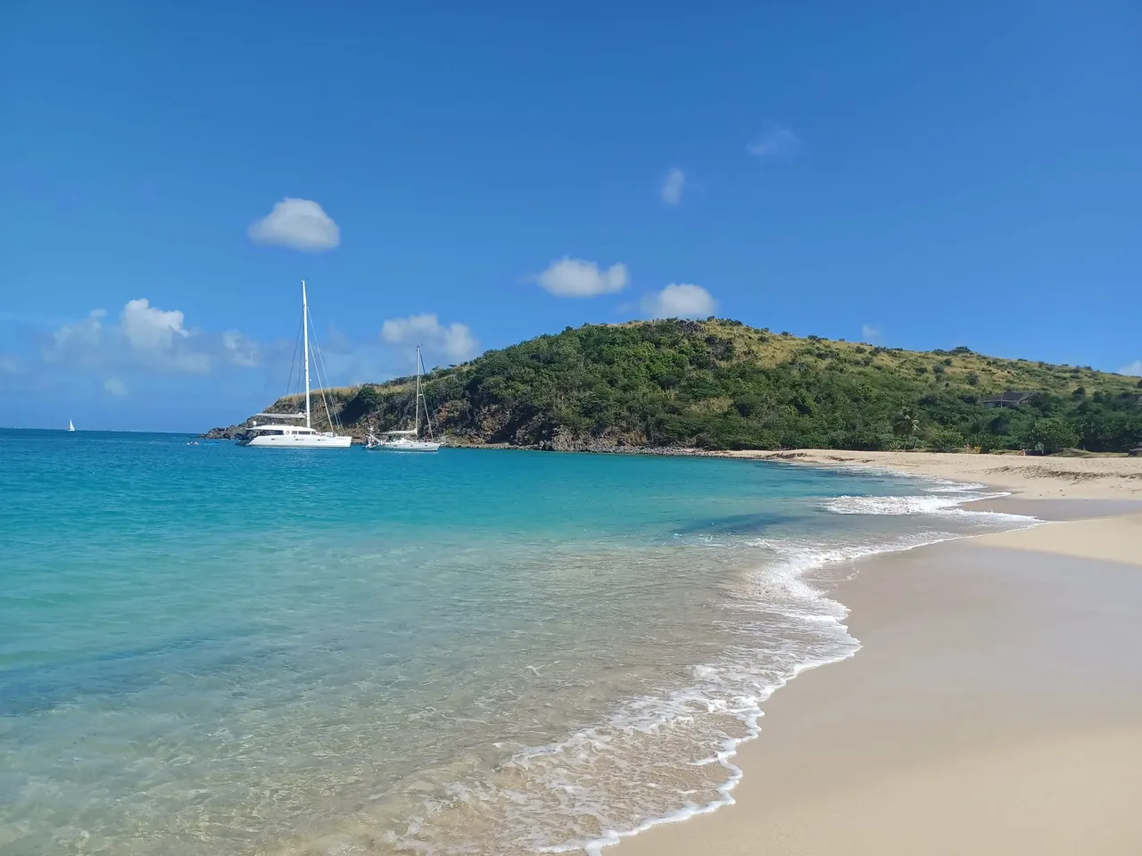 A yacht anchored off a quiet beach on Saint-Martin, with a green headland behind