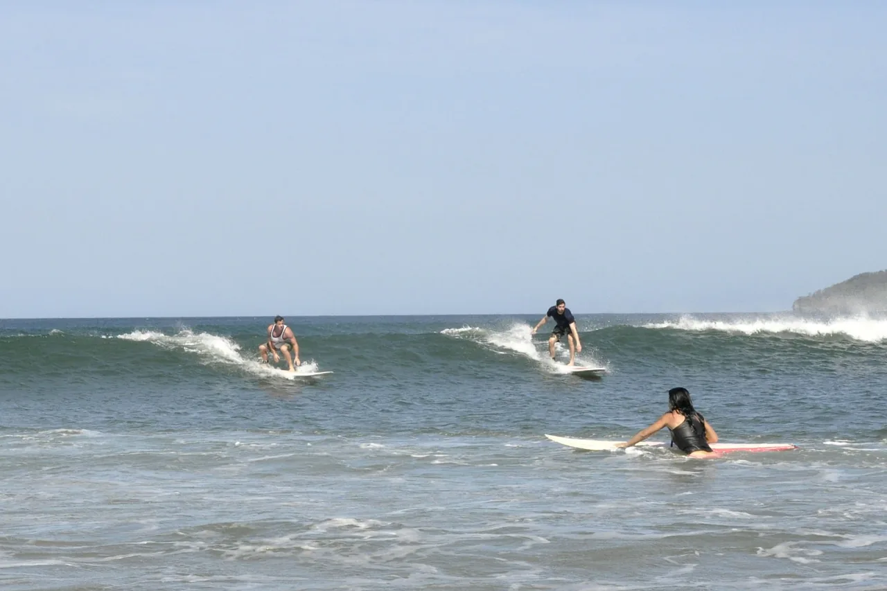 Three surfers paddling and riding small waves in the shallows at Tamarindo
